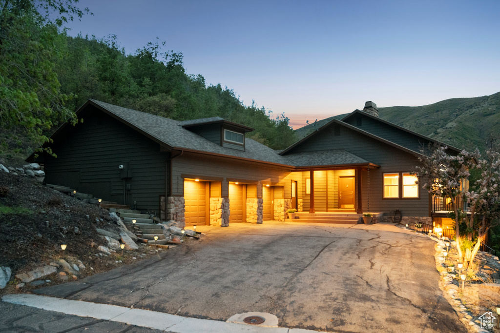 View of front of house featuring asphalt driveway, a garage, a porch, a chimney, and stone siding