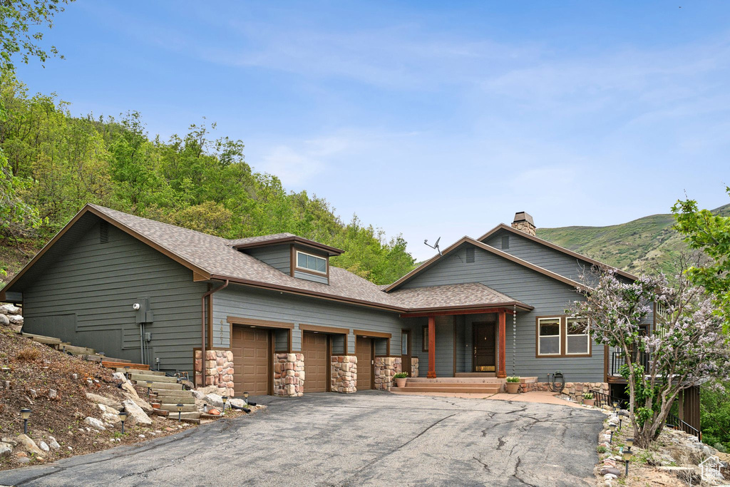 View of front of house featuring an attached garage, asphalt driveway, a shingled roof, a chimney, and stone siding