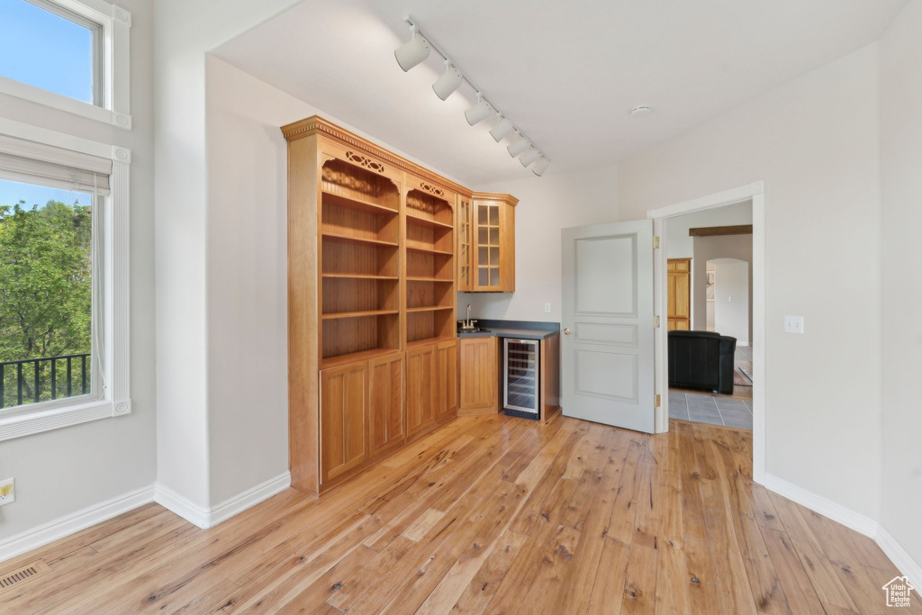 Bar area featuring beverage cooler, track lighting, light wood-style flooring, baseboards, and a sink