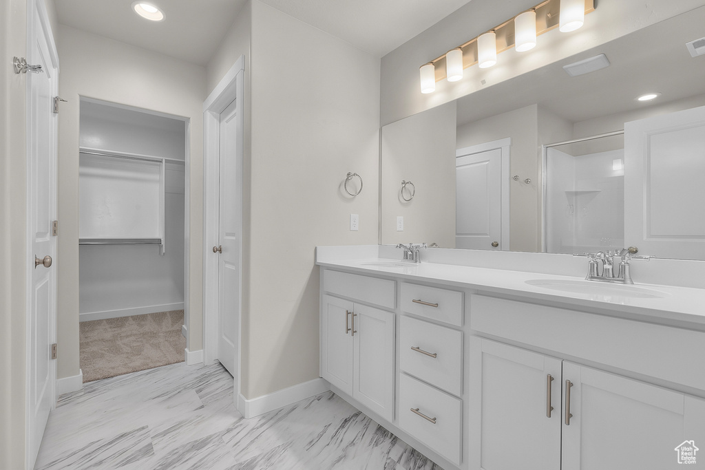 Bathroom featuring baseboards, double vanity, marble look tile flooring, a shower, and a spacious closet