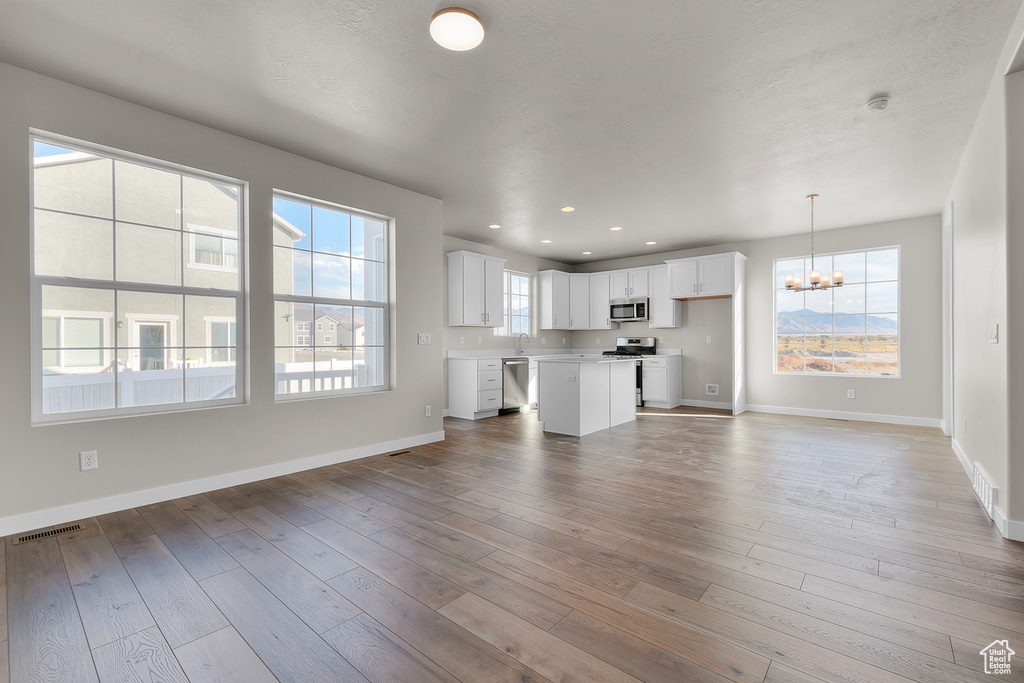 Unfurnished living room with a chandelier, baseboards, light wood-style floors, and recessed lighting
