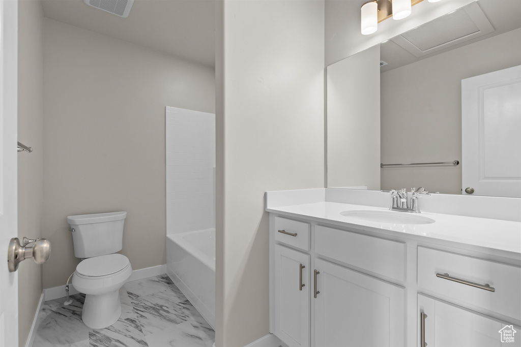 Bathroom with toilet, marble look tiles, baseboards, vanity, and a bath