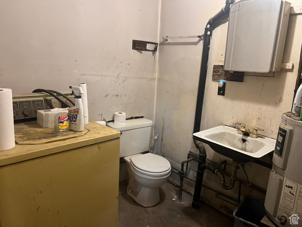Bathroom with unfinished concrete flooring, a sink, toilet, and water heater