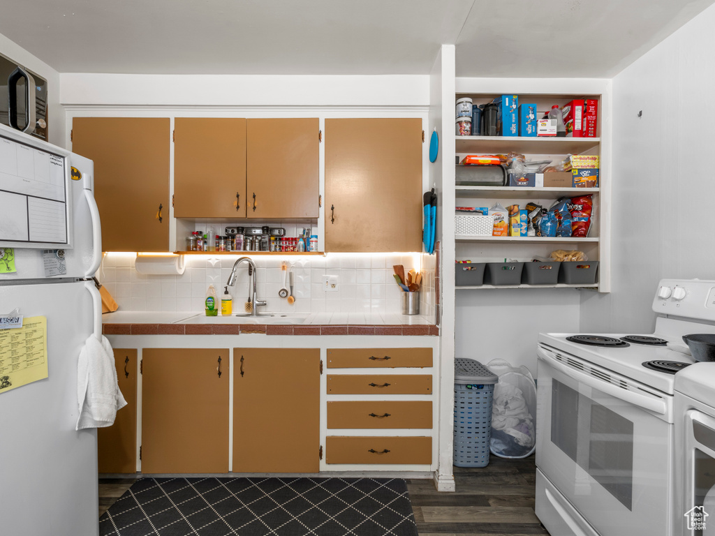 Kitchen featuring white appliances, a sink, tile countertops, dark wood finished floors, and decorative backsplash