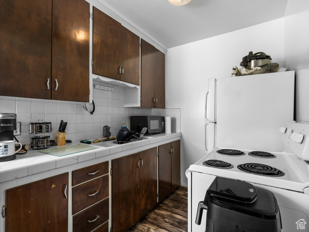 Kitchen featuring white appliances, tile countertops, dark brown cabinets, and dark wood-style flooring