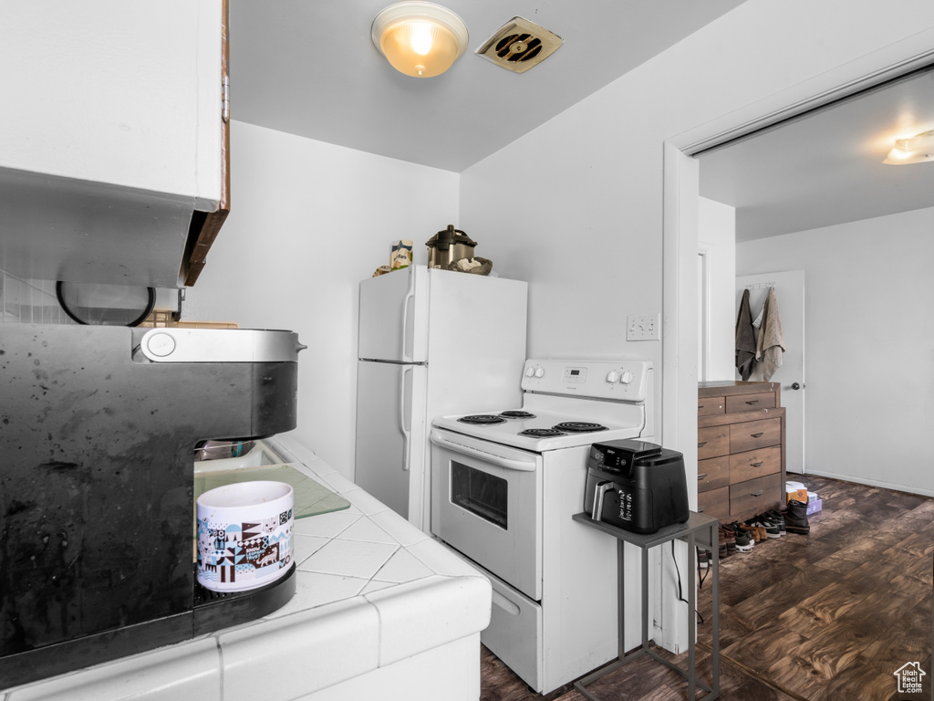 Kitchen with white appliances, tile countertops, white cabinetry, and dark wood-style floors