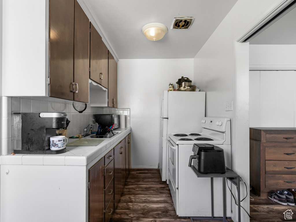 Kitchen with electric stove, tile countertops, backsplash, dark wood-type flooring, and dark brown cabinets