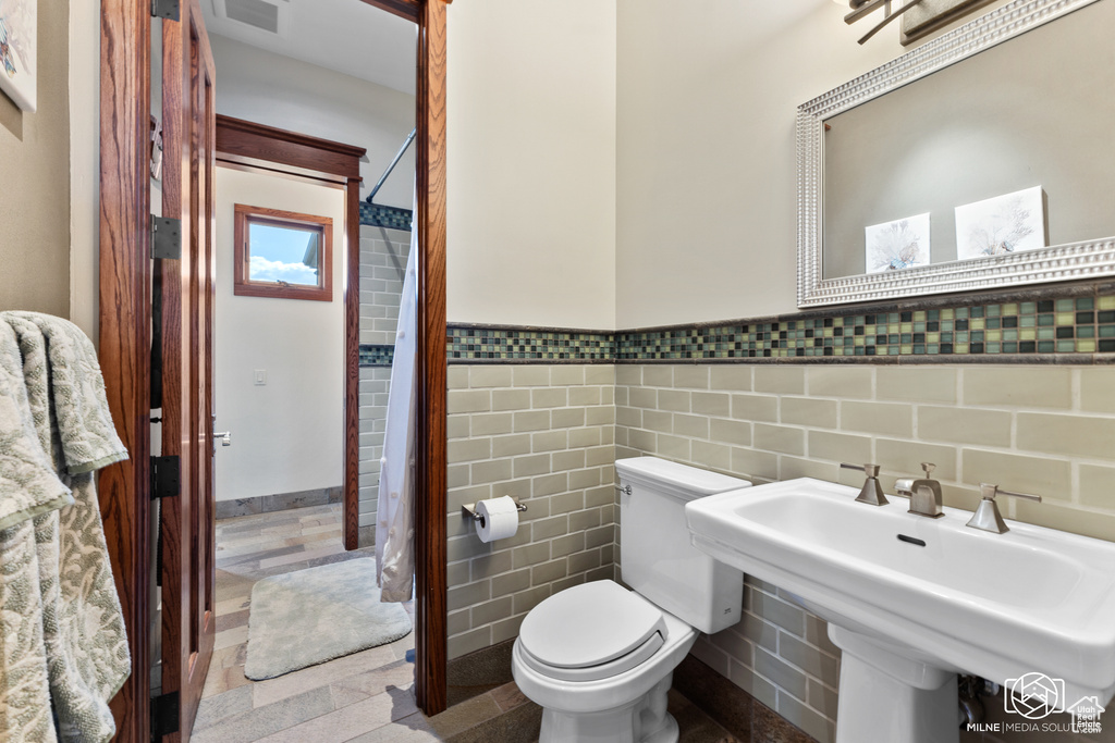 Full bathroom featuring tile walls, toilet, a wainscoted wall, a sink, and a shower