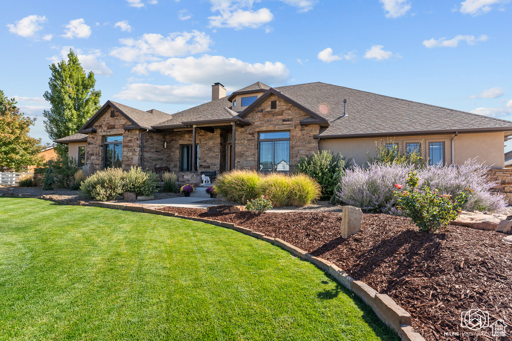 View of front of home with a front lawn, stone siding, a chimney, and roof with shingles