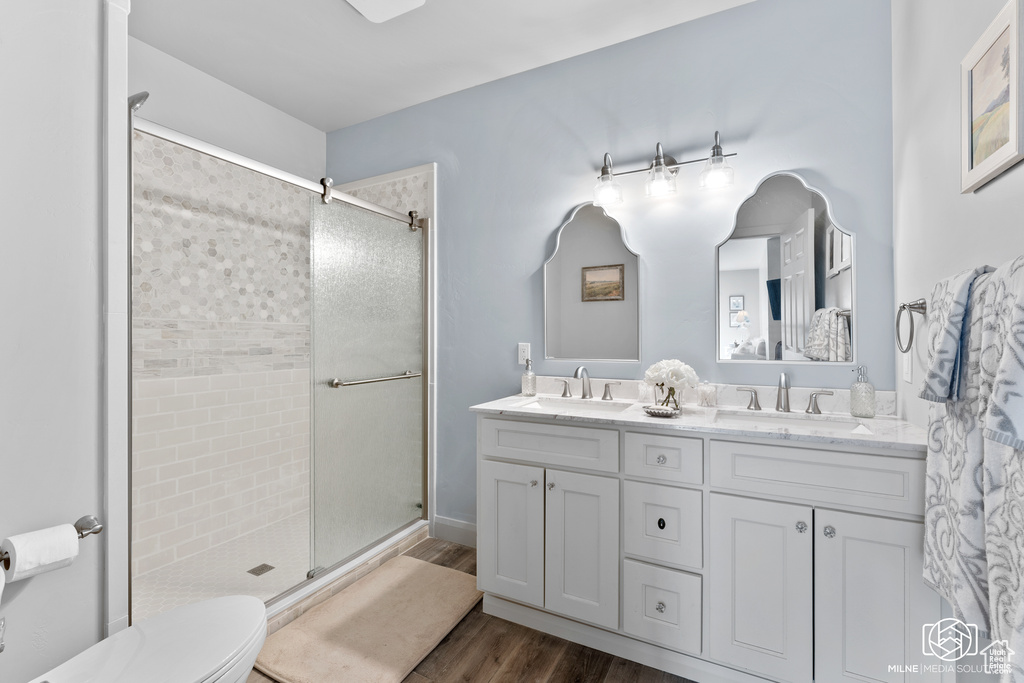 Bathroom with a stall shower, wood finished floors, double vanity, and toilet