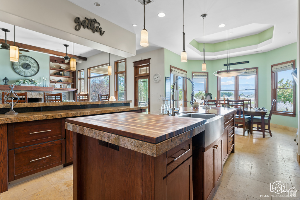 Kitchen with butcher block countertops, a kitchen island with sink, recessed lighting, a raised ceiling, and pendant lighting