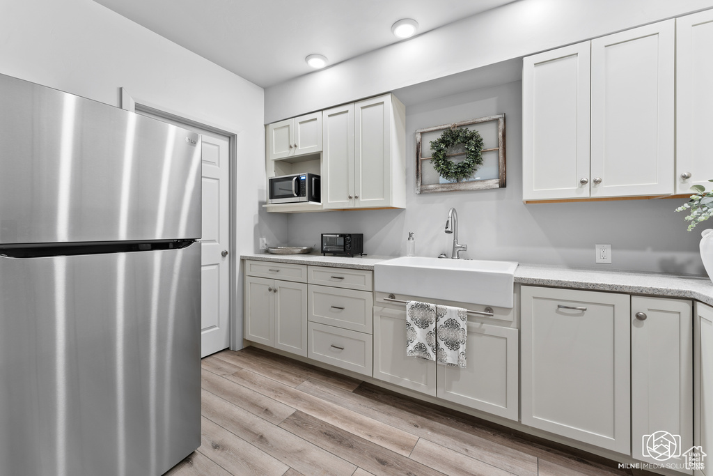 Kitchen with stainless steel appliances, a sink, light countertops, light wood-type flooring, and white cabinets