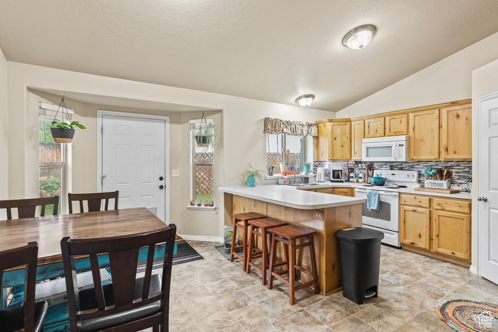 Kitchen featuring white appliances, a peninsula, light countertops, tasteful backsplash, and a kitchen breakfast bar