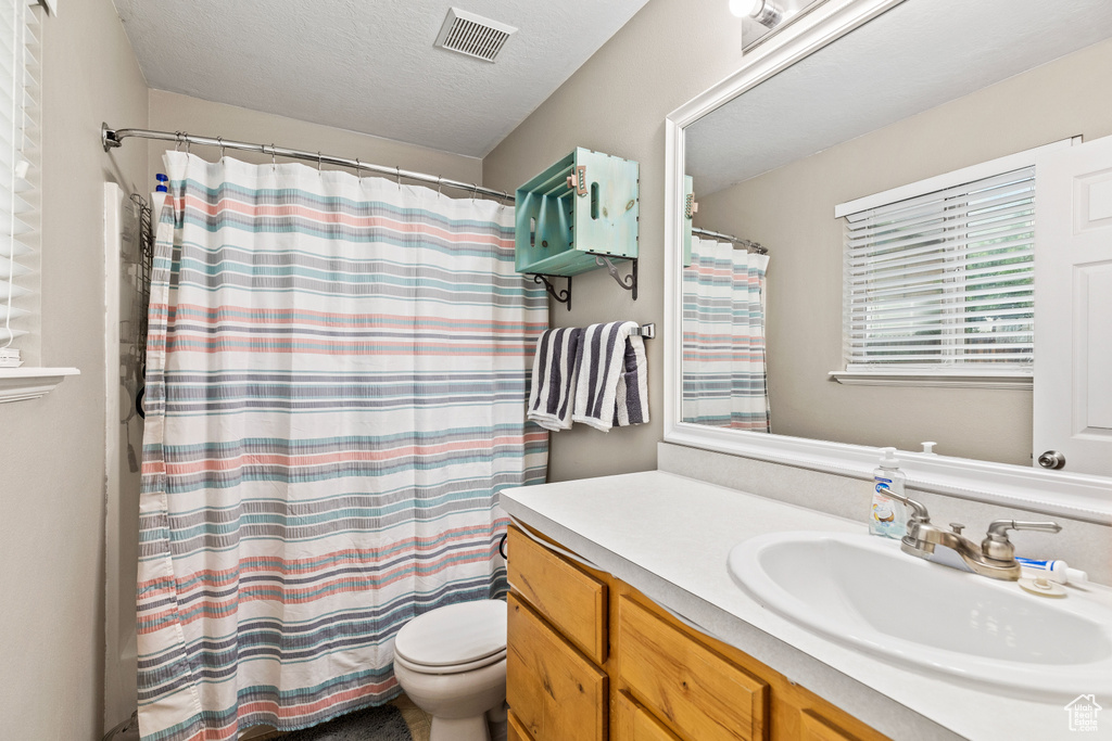 Bathroom with toilet, vanity, curtained shower, and a textured ceiling