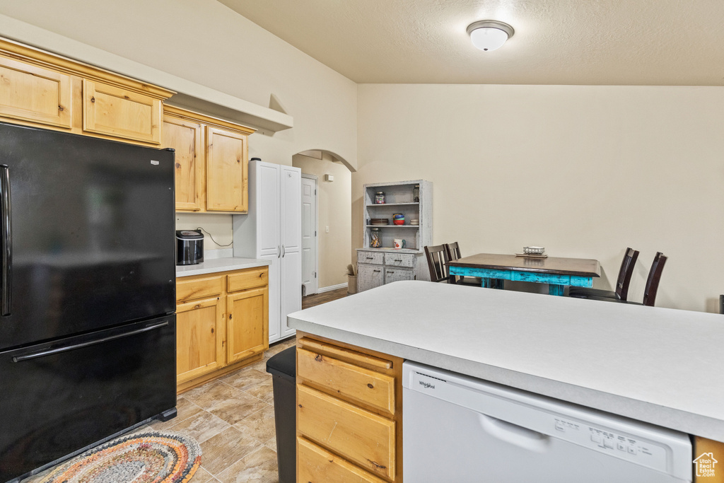 Kitchen with freestanding refrigerator, white dishwasher, light brown cabinetry, arched walkways, and light countertops