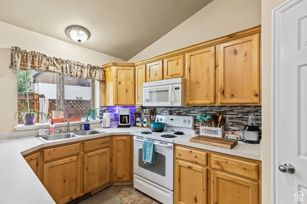Kitchen with white appliances, a sink, light countertops, backsplash, and lofted ceiling