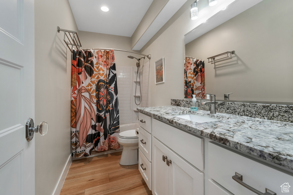Full bath featuring vanity, wood finished floors, toilet, shower / bath combination with curtain, and recessed lighting