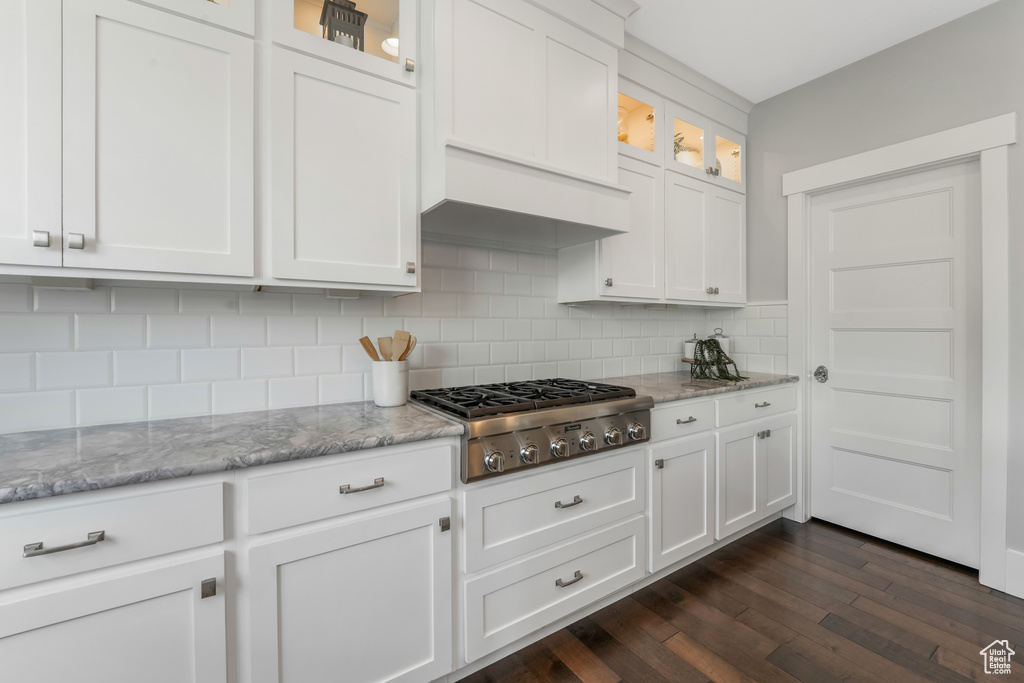 Kitchen with stainless steel gas stovetop, backsplash, dark wood-type flooring, white cabinets, and glass insert cabinets