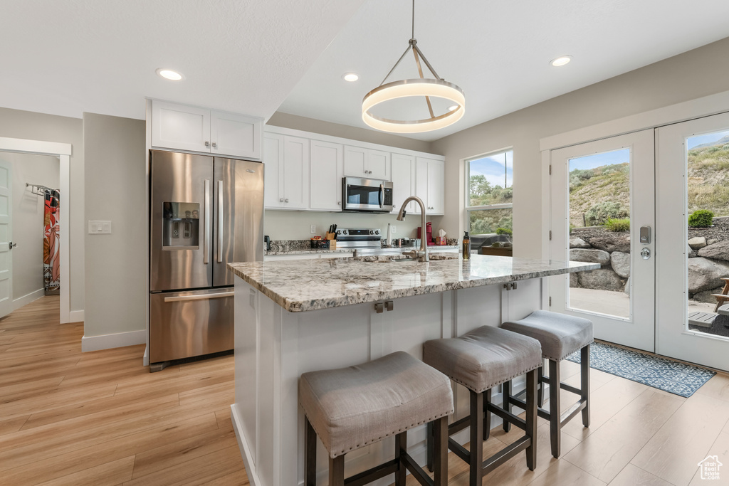 Kitchen featuring stainless steel appliances, light wood-type flooring, recessed lighting, a sink, and a breakfast bar area