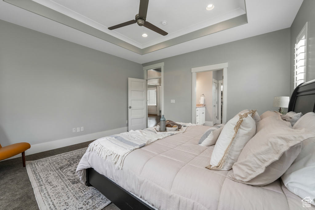 Carpeted bedroom featuring a raised ceiling, baseboards, recessed lighting, ensuite bath, and ceiling fan