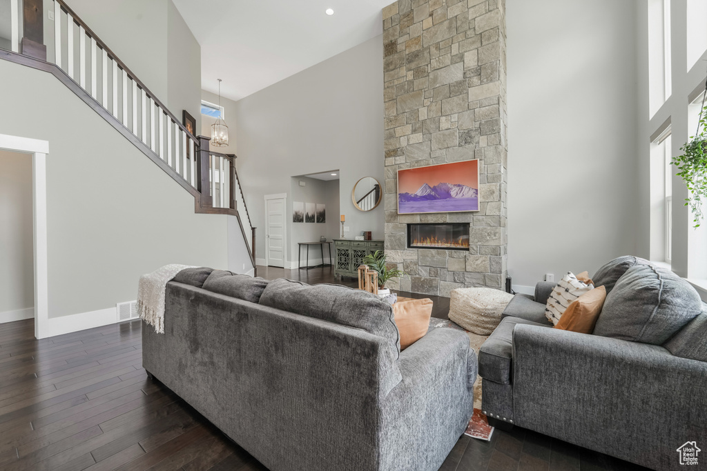 Living area with a towering ceiling, stairs, a stone fireplace, dark wood finished floors, and baseboards