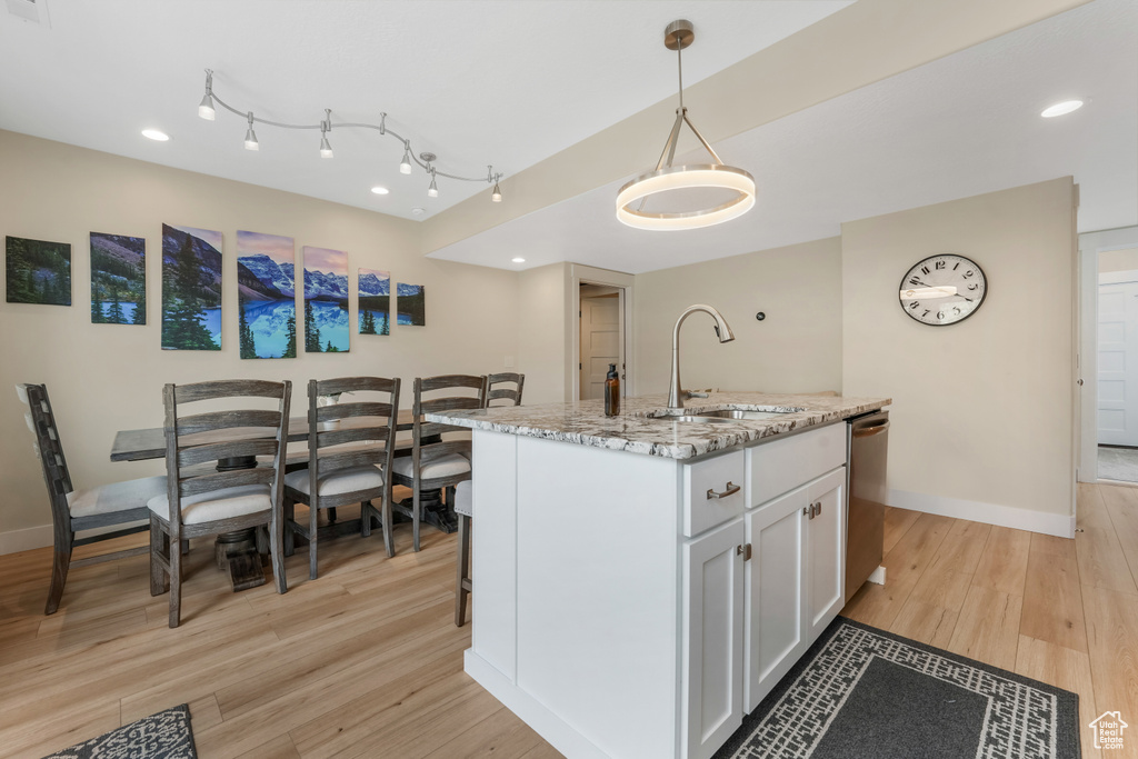 Kitchen with a sink, light wood finished floors, white cabinets, baseboards, and recessed lighting
