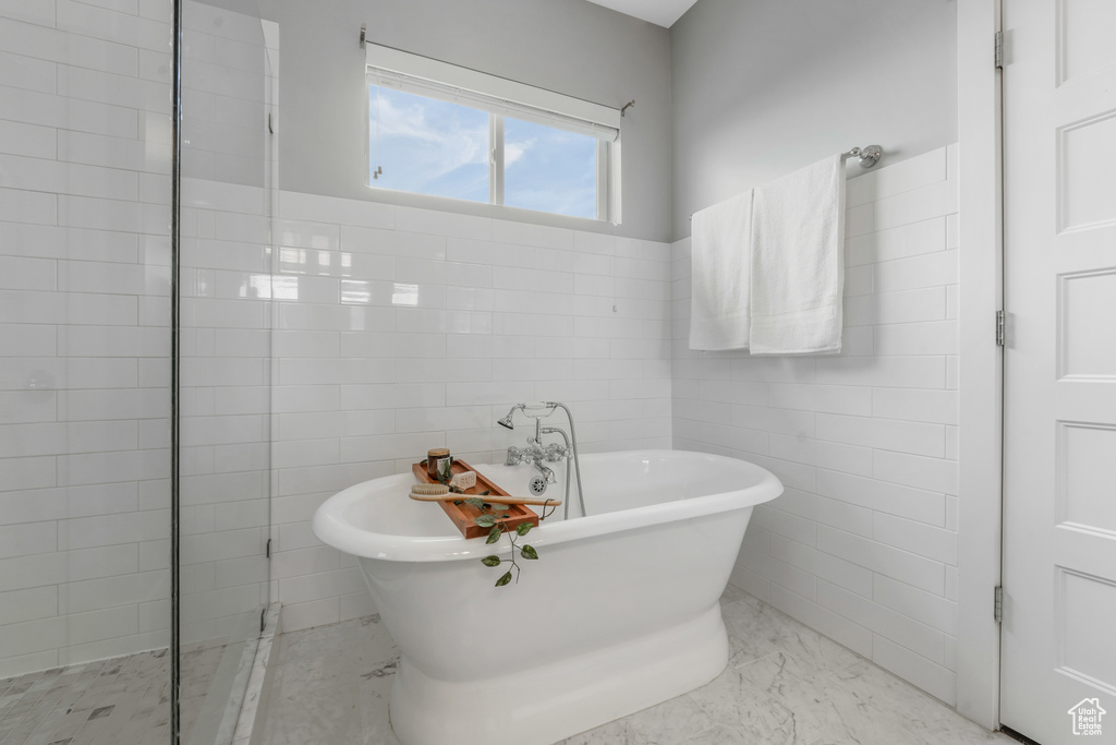 Bathroom with a freestanding bath, tile walls, marble finish flooring, and a tile shower
