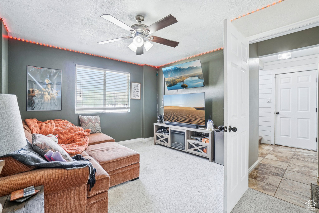 Carpeted living area with a ceiling fan, baseboards, and a textured ceiling