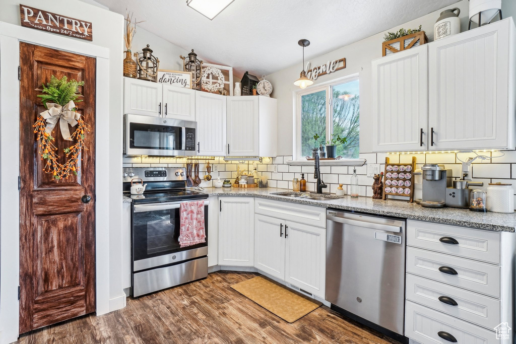 Kitchen with stainless steel appliances, lofted ceiling, decorative backsplash, a sink, and white cabinetry