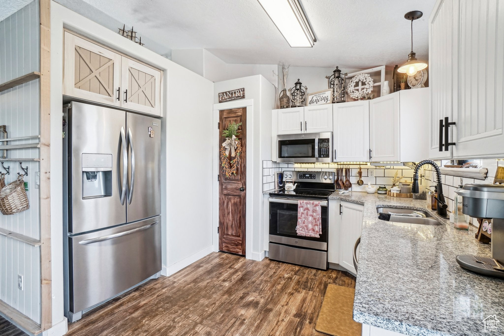 Kitchen featuring stainless steel appliances, a sink, dark wood-type flooring, decorative backsplash, and light stone counters