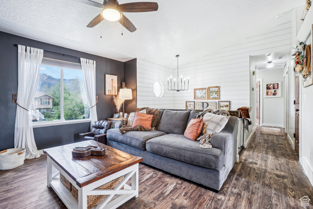 Living room with dark wood-type flooring, baseboards, a chandelier, a textured ceiling, and wood walls