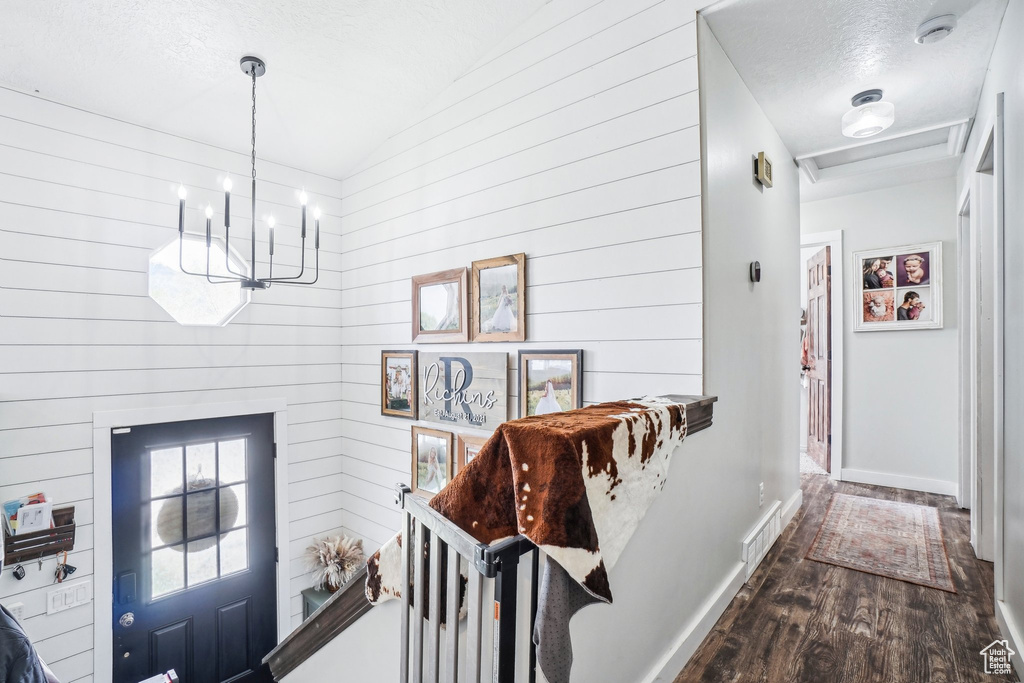 Interior space featuring a chandelier, dark wood finished floors, wood walls, baseboards, and a textured ceiling