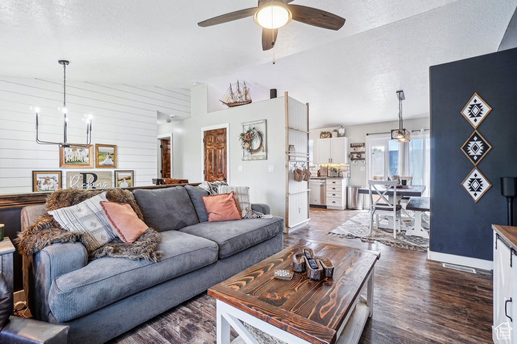 Living area with a chandelier, dark wood-style flooring, a ceiling fan, a textured ceiling, and lofted ceiling