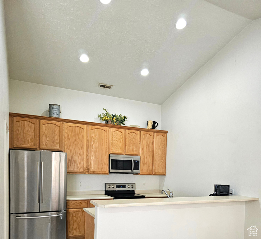 Kitchen featuring stainless steel appliances, recessed lighting, lofted ceiling, light countertops, and brown cabinetry