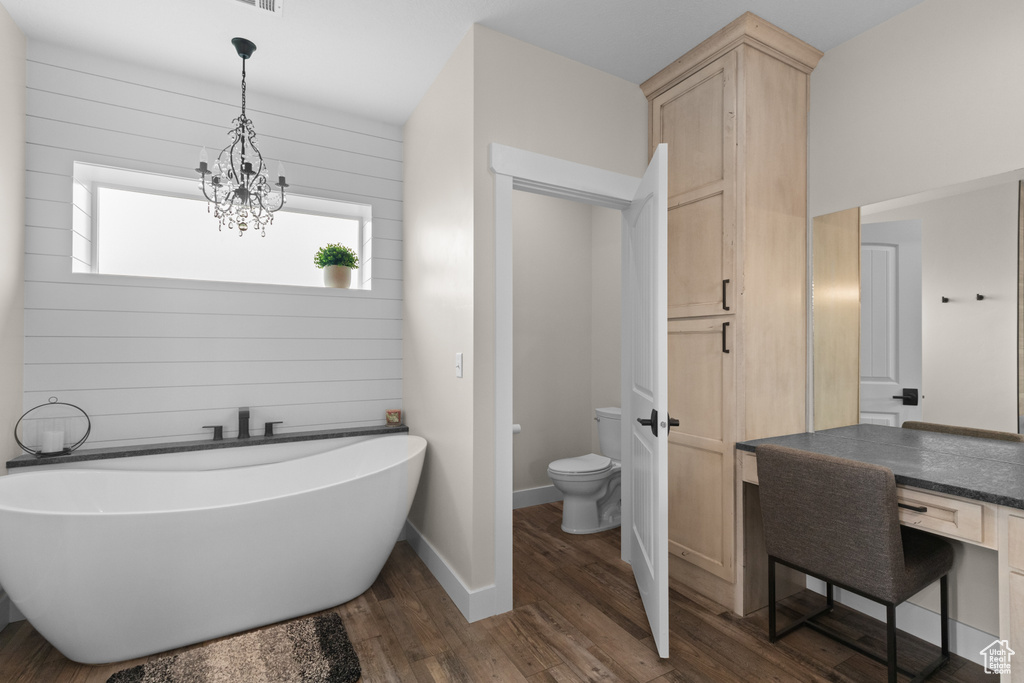 Bathroom with toilet, wood finished floors, a freestanding bath, a chandelier, and baseboards