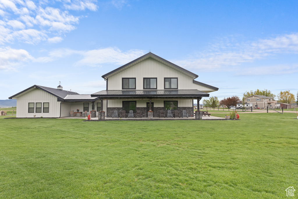 Back of house featuring a lawn, a patio area, metal roof, and stone siding