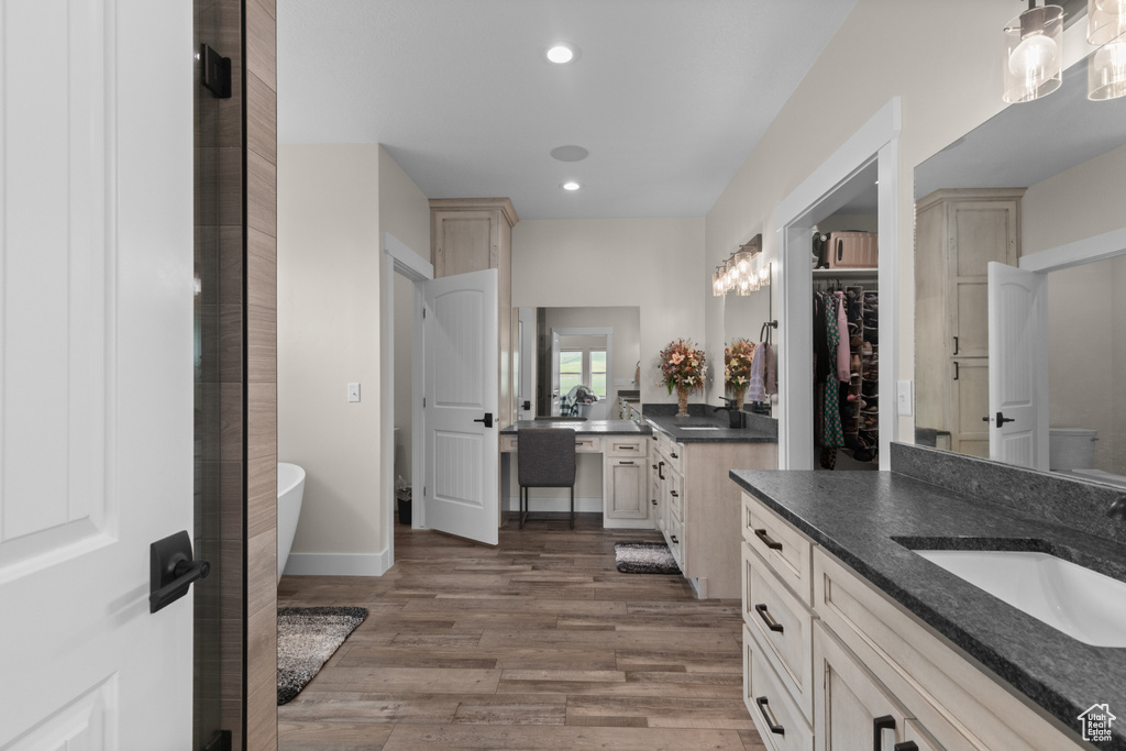Full bathroom featuring two vanities, wood finished floors, a soaking tub, recessed lighting, and baseboards