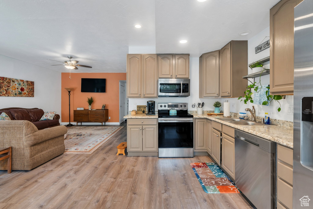 Kitchen featuring stainless steel appliances, a sink, a ceiling fan, light wood-style floors, and open floor plan