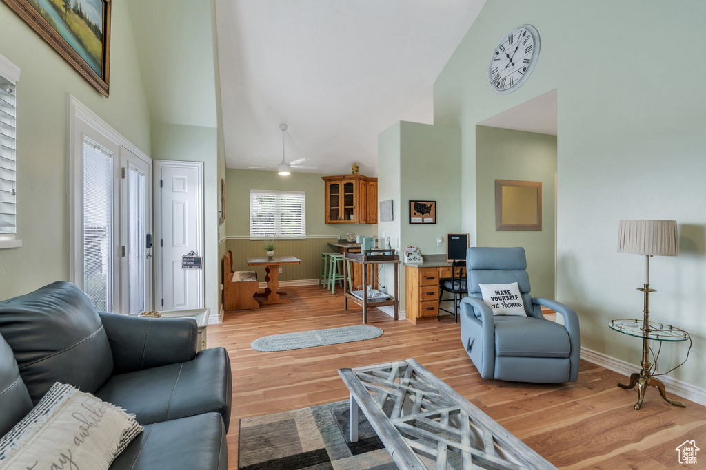 Living area featuring high vaulted ceiling, light wood finished floors, baseboards, and a ceiling fan