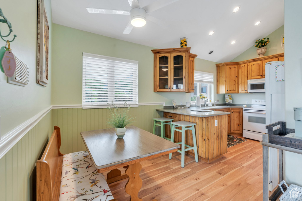 Kitchen featuring white appliances, wainscoting, a peninsula, glass insert cabinets, and light wood finished floors