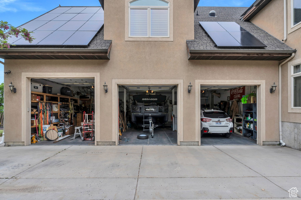 Back of property featuring concrete driveway, an attached garage, stucco siding, and roof mounted solar panels