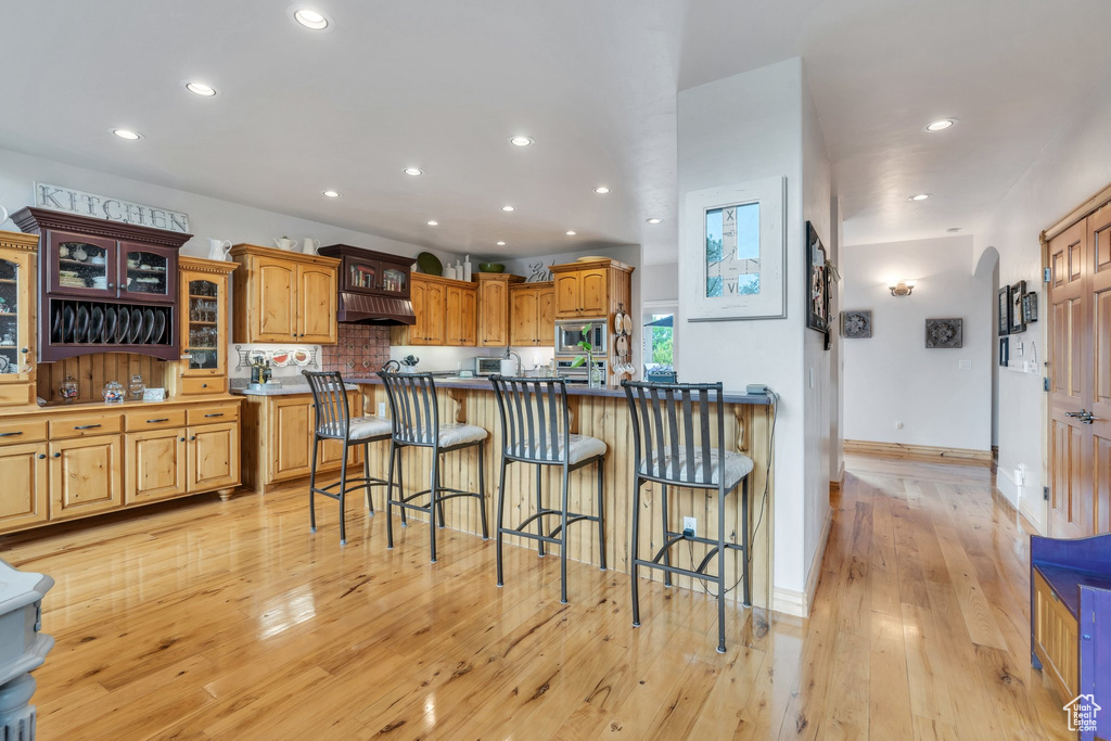 Kitchen featuring stainless steel microwave, a kitchen bar, recessed lighting, light wood-style flooring, and glass insert cabinets