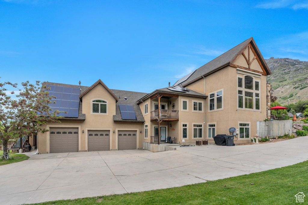 Rear view of house featuring a balcony, driveway, stucco siding, a garage, and roof mounted solar panels