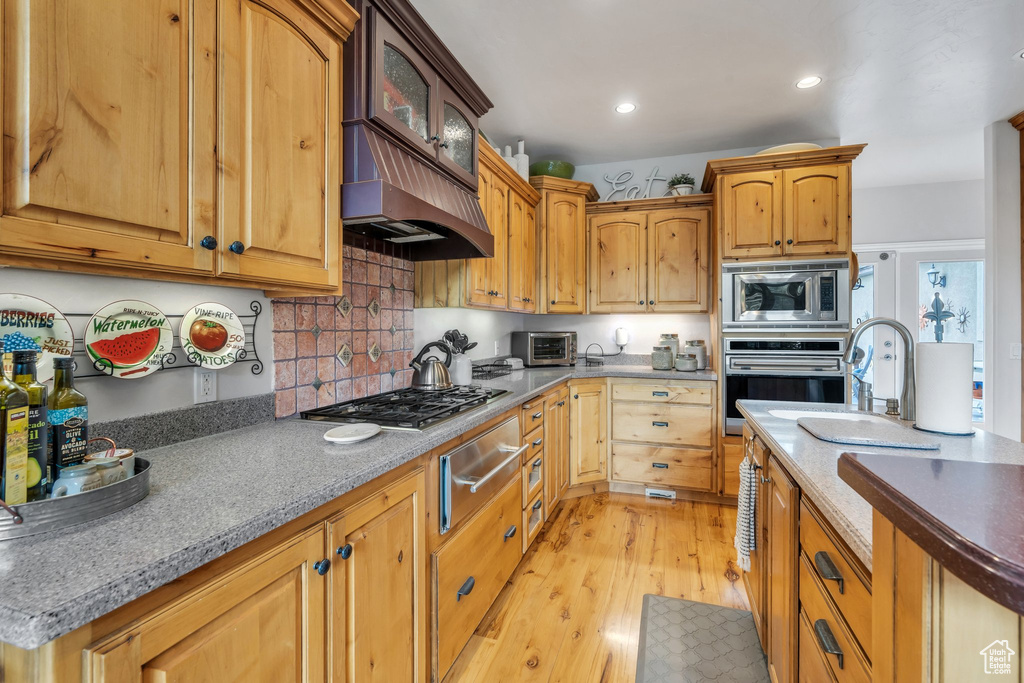 Kitchen featuring stainless steel appliances, a warming drawer, light wood-style flooring, glass insert cabinets, and decorative backsplash