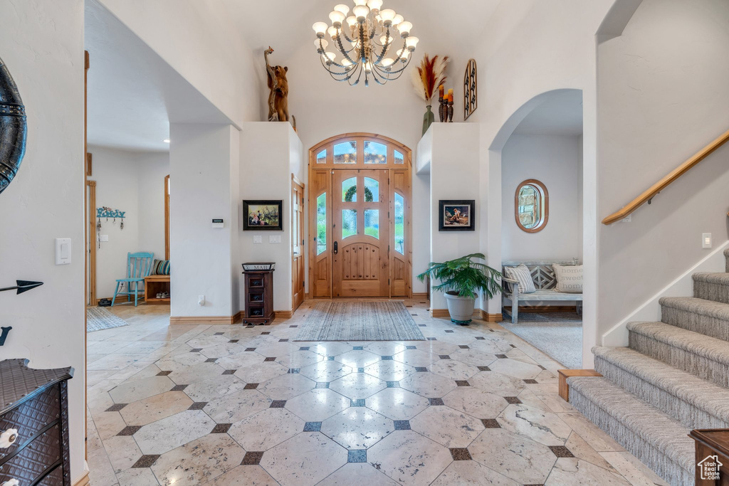 Foyer with arched walkways, a towering ceiling, a chandelier, and stairway
