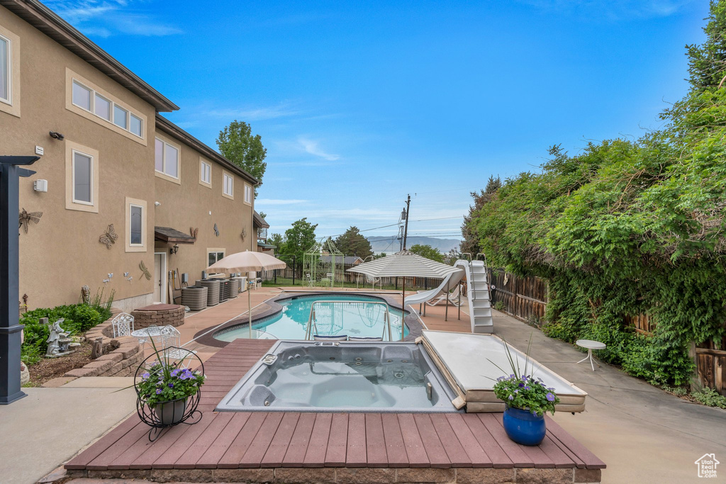 View of swimming pool with a water slide, an in-ground hot tub, a fenced backyard, and a patio area