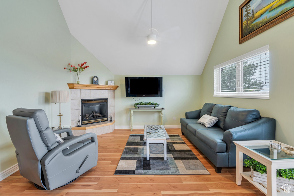 Living area with lofted ceiling, a tile fireplace, baseboards, wood finished floors, and a ceiling fan