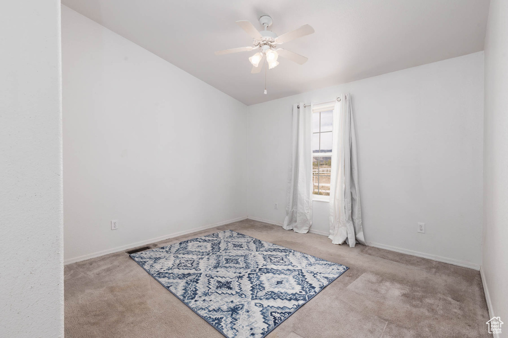 Carpeted empty room with ceiling fan, baseboards, and lofted ceiling