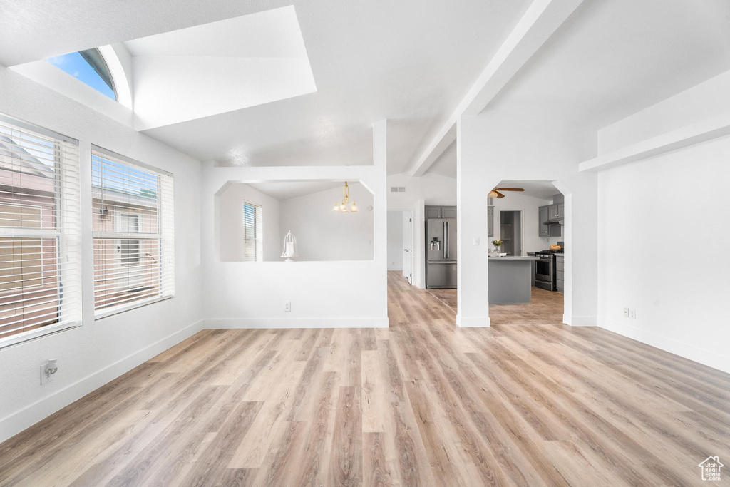 Unfurnished living room with a chandelier, light wood-style flooring, baseboards, and lofted ceiling