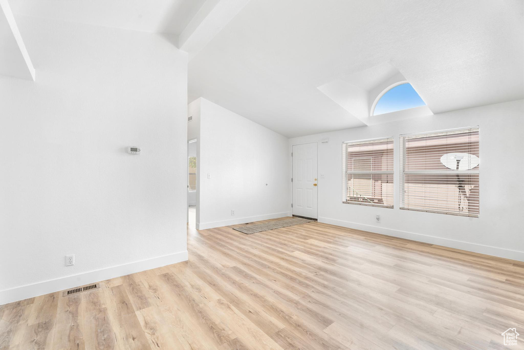 Unfurnished living room featuring lofted ceiling, baseboards, and wood finished floors